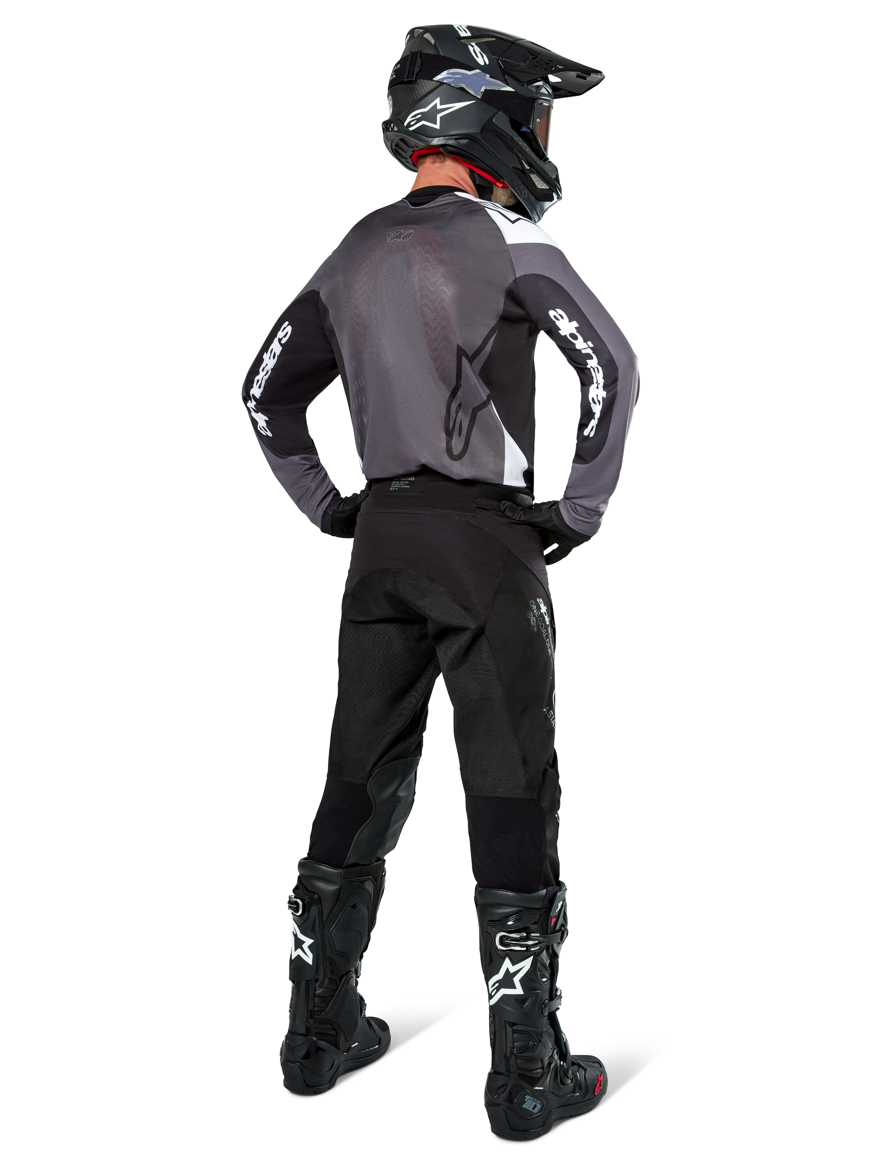 Pilota di motocross con maglia Alpinestars Pro-Dura in Black Magnet White, vista posteriore con pannello in mesh grigio e maniche nere con marchio Alpinestars bianco, coordinata con pantaloni neri, casco nero e stivali neri e bianchi, equipaggiamento professionale da enduro