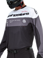 Maglia Alpinestars Pro-Dura, maglia da motocross ed enduro, nero, grigio magnet e bianco, abbigliamento tecnico off-road con perforazioni tagliate al laser e costruzione in tessuto poliestere traspirante.