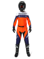 Pilota di motocross con abbigliamento completo Alpinestars Pro-Dura, maglia Navy Hot Orange e bianca, pantaloni coordinati arancioni e navy, stivali da motocross neri con loghi bianchi, casco e guanti neri, completo coordinato per corse fuoristrada