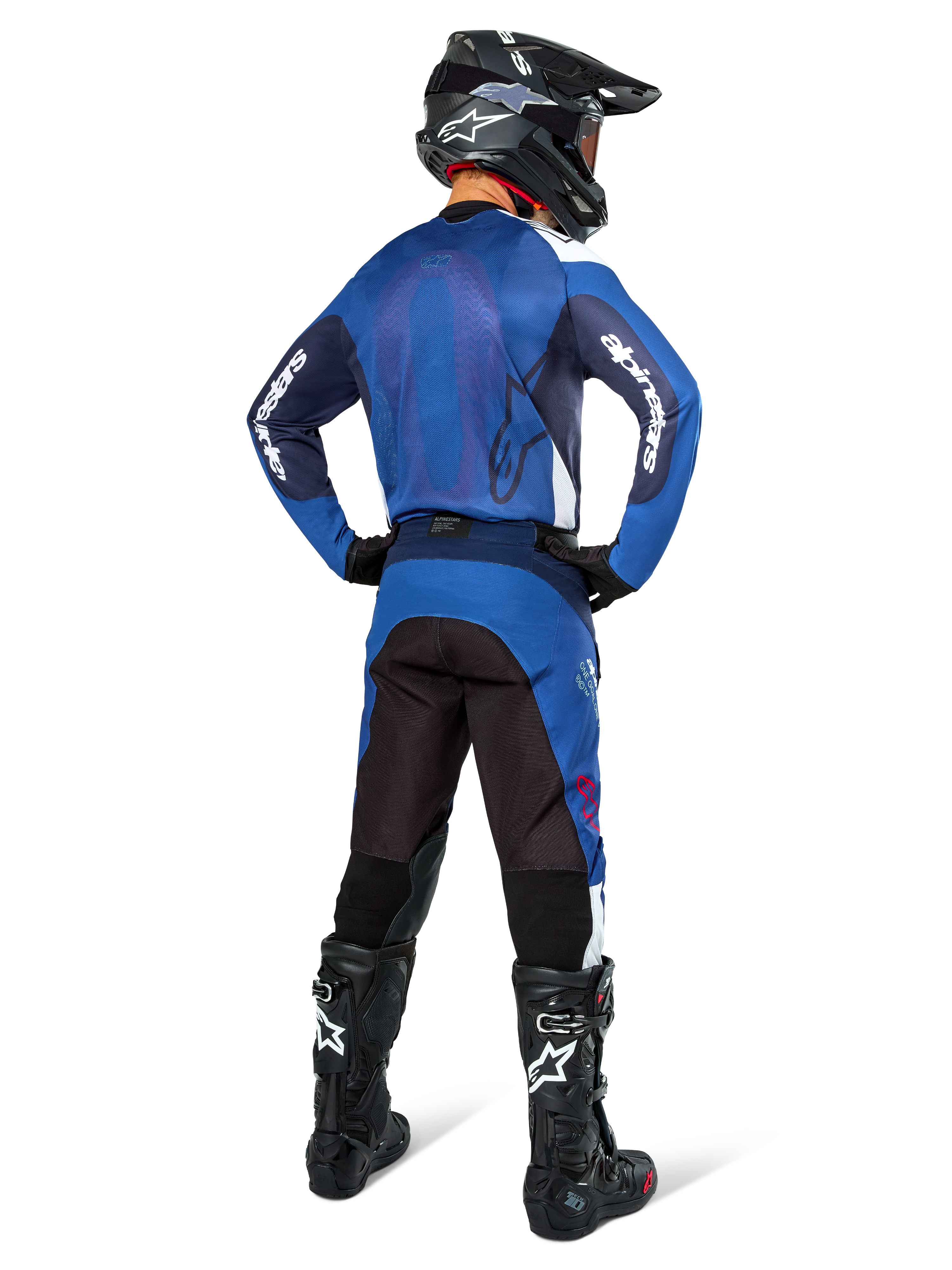 Pilota di motocross visto da dietro che indossa la maglia Alpinestars Pro-Dura in blu navy e blu brillante, pantaloni coordinati blu e neri, casco da motocross nero con maschera e stivali neri, completo da corsa off-road coordinato
