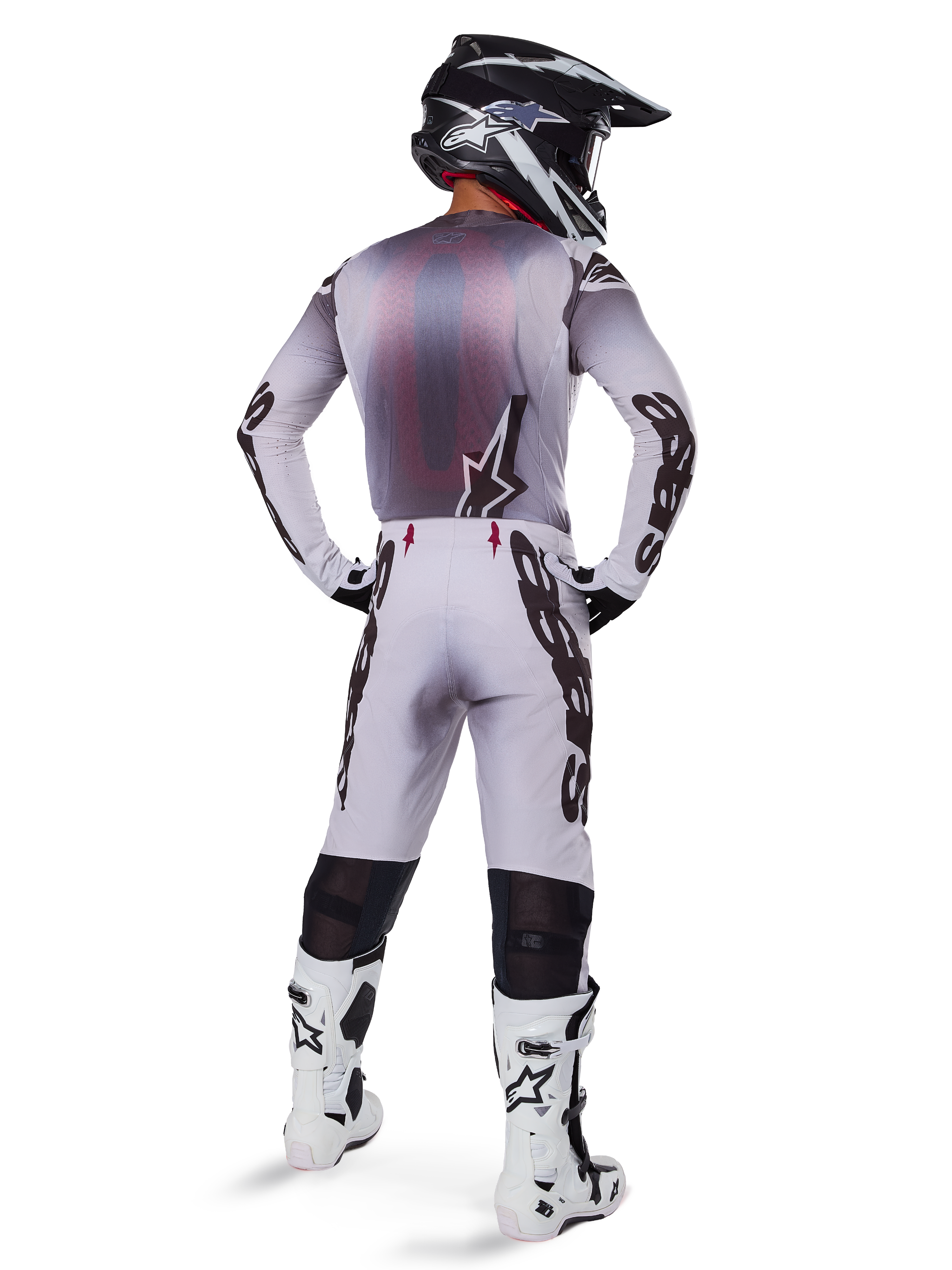 Pilota di motocross con abbigliamento da gara completo, maglia grigia e nera, pantaloni grigio chiaro con marchio 'Astars' nero sui lati, casco nero e bianco, stivali Tech 10 bianchi, completo professionale da gara off-road coordinato