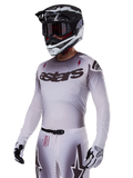 Alpinestars 2025 Supertech Maker Jersey, maglia da motocross, sfumatura argento e nero, mesh elasticizzata traspirante con perforazioni al laser, indossata con pantaloni e casco coordinati, con logo 'astars', equipaggiamento professionale completo da fuoristrada.