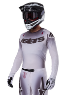 Alpinestars 2025 Supertech Maker Jersey, maglia da motocross, sfumatura argento e nero, mesh elasticizzata traspirante con perforazioni al laser, indossata con pantaloni e casco coordinati, con logo 'astars', equipaggiamento professionale completo da fuoristrada.