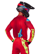 Vista posteriore di un pilota di motocross che indossa il set Alpinestars 2025 Supertech Maker in rosso, caratterizzato da una maglia rossa con grafica giallo neon sulle maniche, pantaloni rossi coordinati, un casco nero con accenti blu e rossi e guanti neri e gialli coordinati.