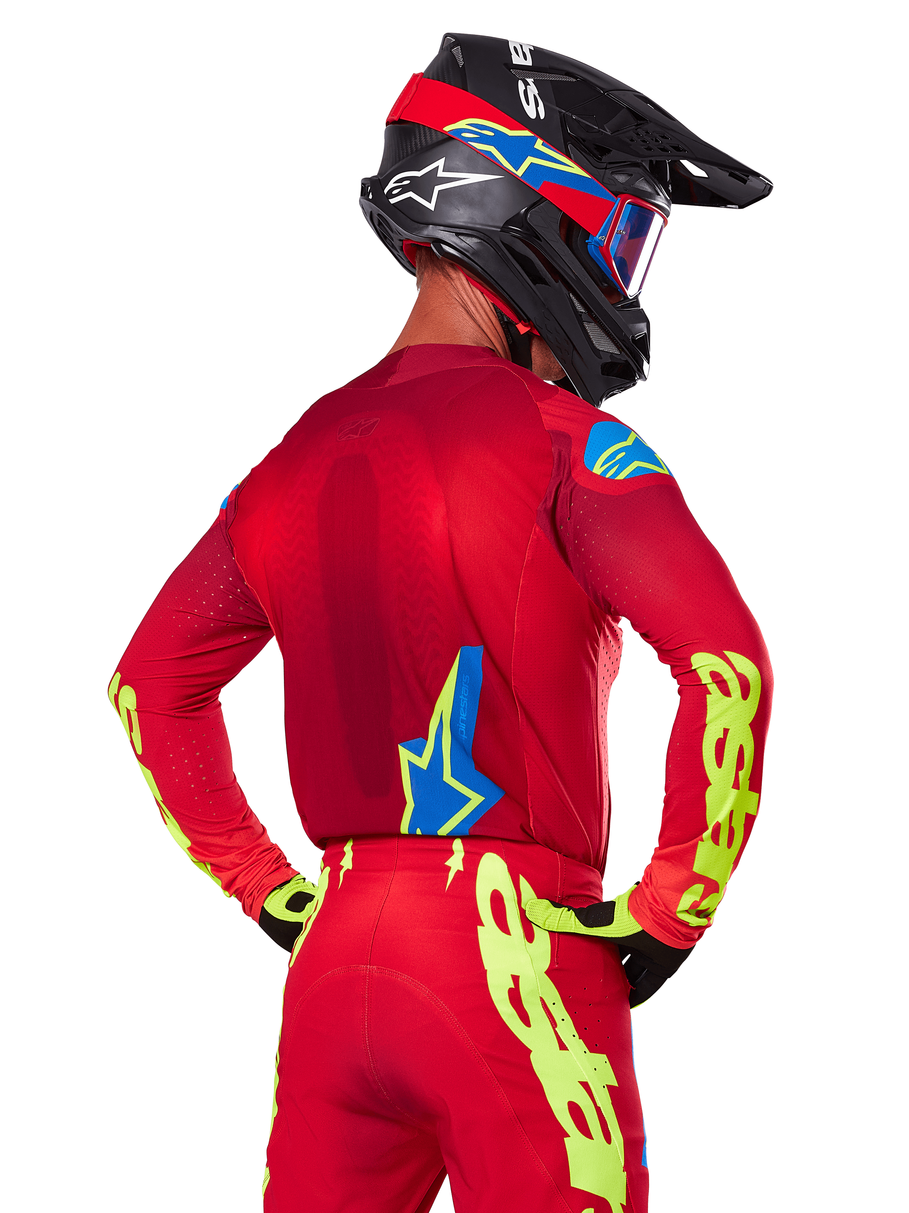 Vista posteriore di un pilota di motocross che indossa il set Alpinestars 2025 Supertech Maker in rosso, caratterizzato da una maglia rossa con grafica giallo neon sulle maniche, pantaloni rossi coordinati, un casco nero con accenti blu e rossi e guanti neri e gialli coordinati.