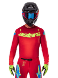 Alpinestars 2025 Supertech Maker Jersey in rosso acceso e giallo fluo, con logo 'astars' giallo sul petto e stelle blu sulle spalle, indossata con pantaloni coordinati, casco nero, maschera blu e guanti gialli, abbigliamento professionale da motocross