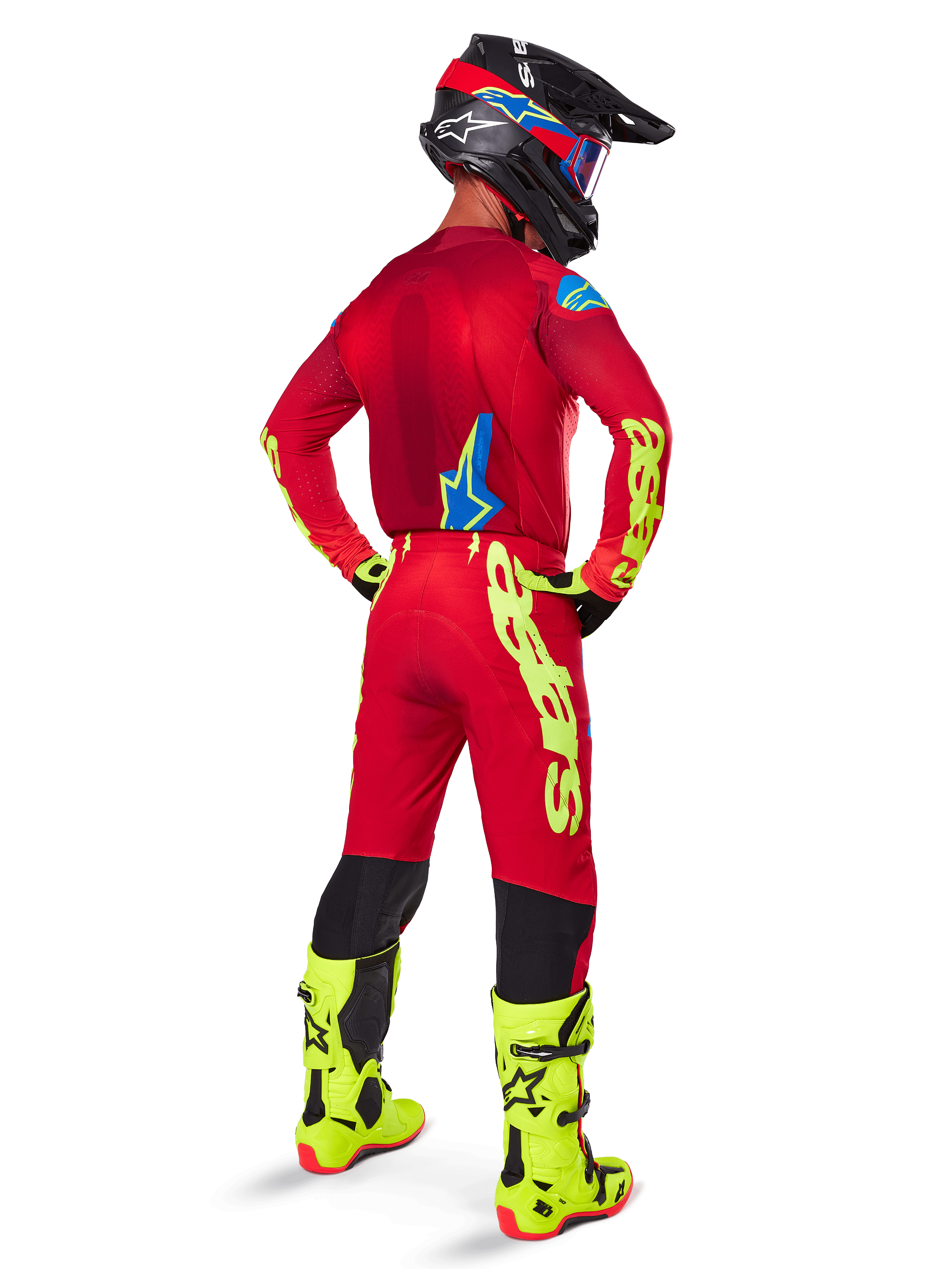 Pilota di motocross visto da dietro, indossa il set Alpinestars 2025 Supertech Maker Gear Set, maglia rosso acceso con logo giallo fluo, pantaloni rossi coordinati con accenti gialli, casco nero con dettagli rossi e blu, stivali giallo fluo, completo da gara professionale per prestazioni fuoristrada