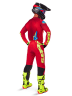 Pilota di motocross visto di spalle che indossa la maglia Alpinestars 2025 Supertech Maker, rosso acceso e giallo fluo, pantaloni coordinati con loghi gialli, stivali giallo fluo e casco nero e rosso, outfit coordinato per corse off-road di livello professionale