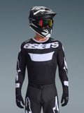 Alpinestars 2026 Racer Air Riway Jersey, maglia da motocross, nero e bianco con marchio 'astars', indossata da un pilota con casco nero, occhiali e pantaloni coordinati, dotata di pannelli in mesh traspirante per corse off-road.