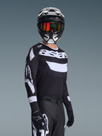 Pilota di motocross che indossa la maglia Alpinestars Racer Air Riway 2026, maglia bianca e nera con logo 'astars', casco coordinato bianco e nero con maschera a specchio arancione, pantaloni e guanti da motocross neri, outfit coordinato per gare off-road