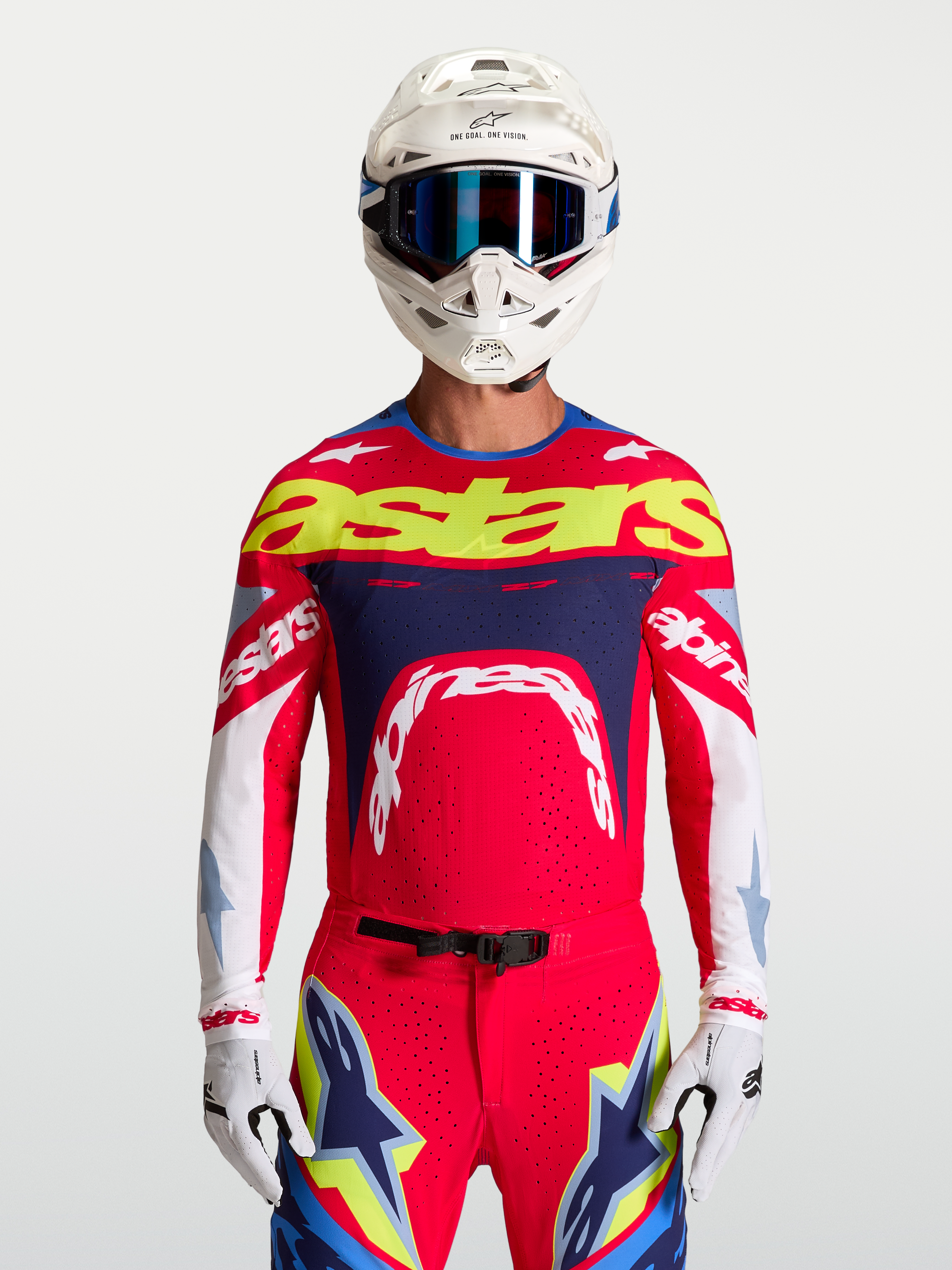 Alpinestars maglia Supertech Dyna, maglia da motocross da uomo, rosso e blu navy con logo giallo, in rete elasticizzata traspirante e vestibilità atletica, indossata da un pilota con casco e guanti, abbigliamento tecnico per off-road
