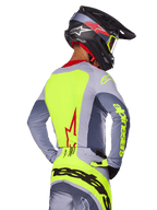 Alpinestars 2025 Techstar Melt Jersey, Bright Red Gray, vista posteriore di un pilota di motocross con abbigliamento da gara grigio e giallo neon, logo a stella rossa sulla schiena, casco coordinato nero e rosso, abbigliamento tecnico per fuoristrada