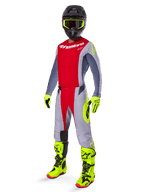 Pilota di motocross con maglia Alpinestars Techstar Melt 2025 in rosso brillante e grigio, caratterizzata da petto rosso e maniche grigie con accenti giallo fluorescente. Abbinata a pantaloni coordinati, stivali da gara e guanti giallo brillante, e casco nero con maschera dalla montatura gialla per un kit completo da gara off-road.