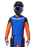 Alpinestars 2025 Techstar Melt Jersey, maglia da motocross, blu e arancione con pannelli laterali neri, indossata con casco nero e occhiali blu, con perforazioni laser traspiranti sul petto, vestibilità atletica da gara per prestazioni fuoristrada