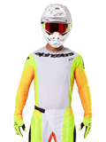 Alpinestars Techstar Melt Jersey 2025, abbigliamento da motocross, petto bianco con maniche giallo fluo e arancioni, pilota con casco bianco e maschera rossa, guanti giallo fluo con loghi neri, colorazione vivace per prestazioni off-road