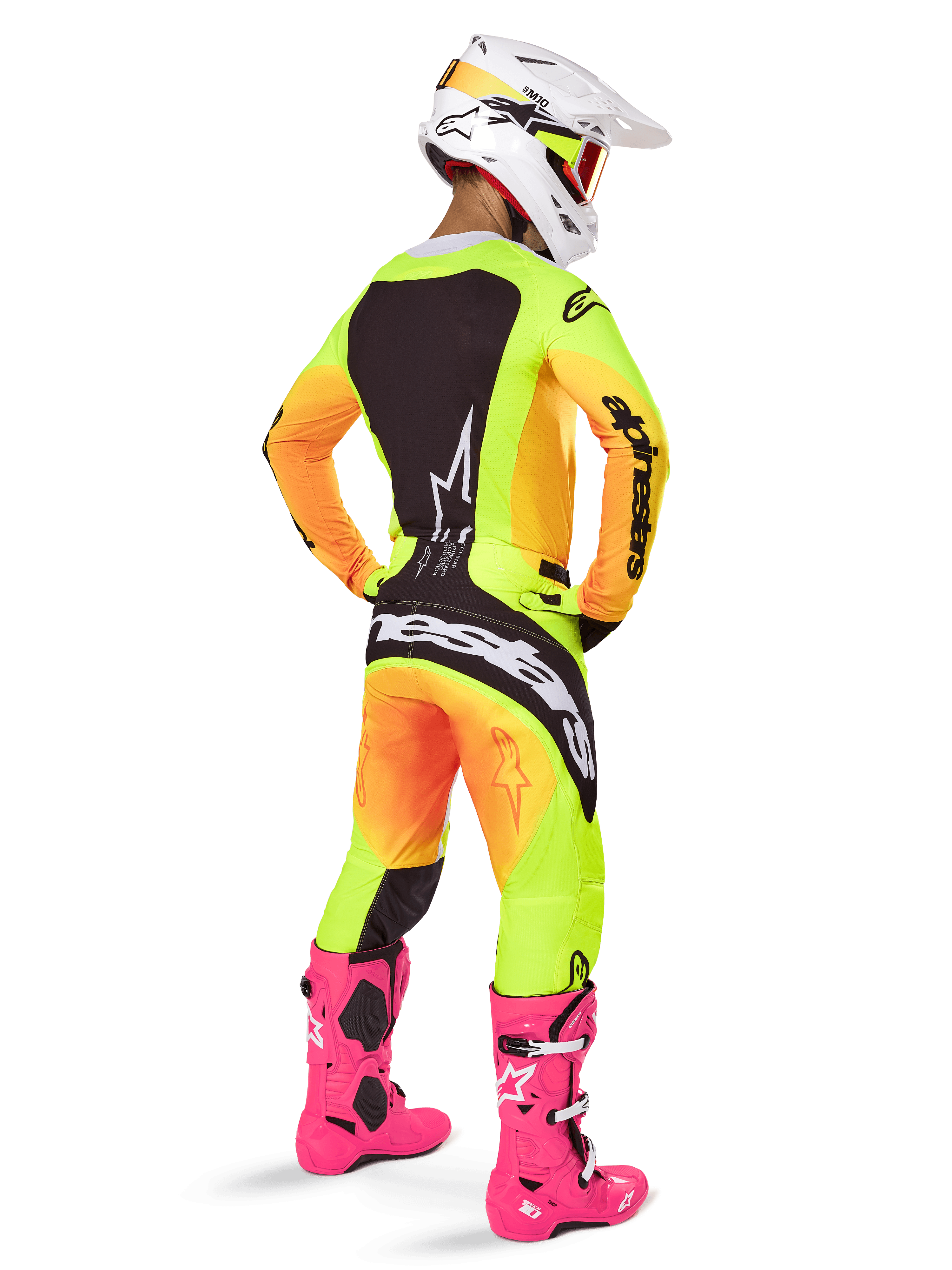 Pilota di motocross visto da dietro, maglia Alpinestars Techstar Melt 2025, sfumatura giallo e arancione vibrante con sezioni nere, pantaloni da motocross coordinati, stivali rosa acceso e casco bianco, vestibilità atletica per competizioni fuoristrada