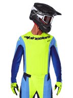 Alpinestars 2025 Techstar Melt Jersey, maglia da motocross, giallo fluo e blu, con ventilazione tagliata al laser e vestibilità atletica da gara, indossata da un pilota con casco nero e guanti giallo fluo