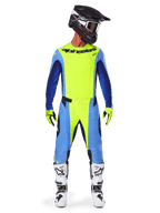 Pilota di motocross con abbigliamento completo da gara, Maglia Alpinestars 2025 Techstar Melt in Giallo Fluo e Blu, pantaloni da motocross coordinati gialli e blu, casco nero con grafiche bianche e occhiali, stivali bianchi e neri, guanti gialli e neri, completo performante coordinato per corse fuoristrada
