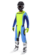 Pilota di motocross con maglia Alpinestars Techstar Melt 2025, giallo fluo e blu, abbinata a pantaloni coordinati, casco nero con maschera, guanti gialli e stivali bianchi e neri, abbigliamento tecnico completo per corse fuori strada