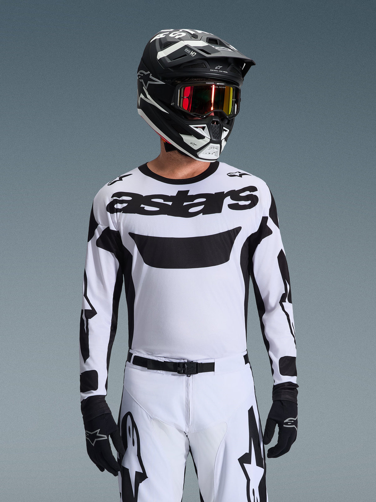 Pilota di motocross che indossa la maglia Alpinestars 2026 Racer Riway in bianco e nero, con logo 'astars' sul petto, abbinata a pantaloni coordinati bianco e nero, casco nero con occhiali e guanti neri, kit coordinato per corse off-road
