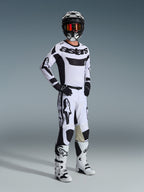 Pilota di motocross con abbigliamento completo da gara, maglia Alpinestars 2026 Racer Riway in bianco e nero, pantaloni da motocross coordinati bianchi e neri, casco nero con occhiali a specchio, stivali bianchi e neri e guanti neri, outfit coordinato per competizioni off-road