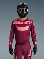 Pilota di motocross con set abbigliamento Alpinestars 2026 Racer Riway, bordeaux e rosa, maglia con branding rosa intenso sul petto, pantaloni coordinati con dettagli neri e rosa, casco integrale nero con maschera e guanti neri, completo da gara off-road coordinato.