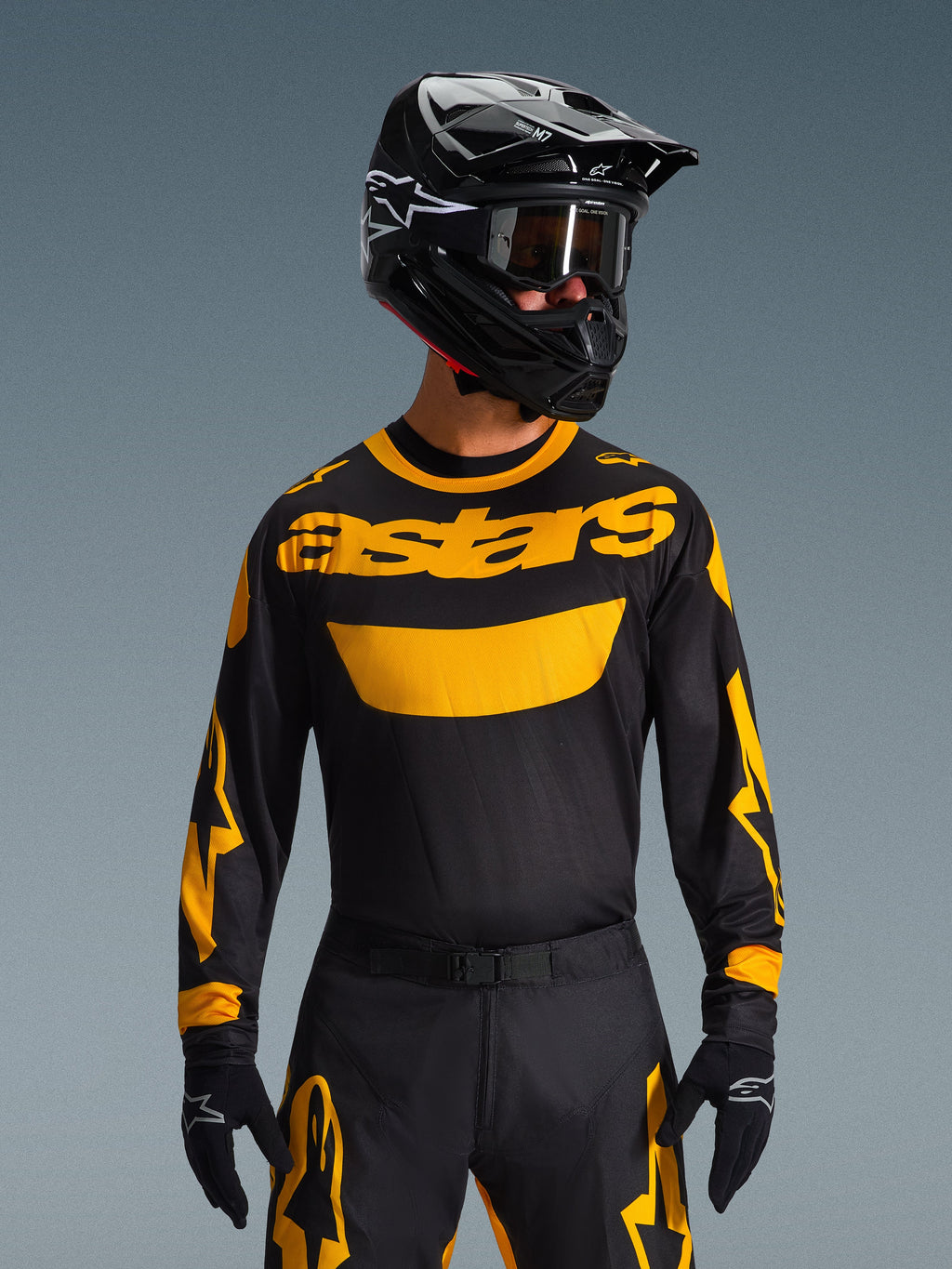 Set Gear Alpinestars Racer Riway 2026, pilota di motocross con maglia nera e vistoso logo 'astars' giallo, pantaloni neri coordinati con dettagli gialli, casco e occhiali neri, guanti neri, abbigliamento professionale da gara fuoristrada