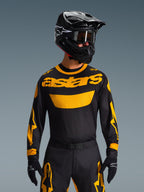 Set Gear Alpinestars Racer Riway 2026, pilota di motocross con maglia nera e vistoso logo 'astars' giallo, pantaloni neri coordinati con dettagli gialli, casco e occhiali neri, guanti neri, abbigliamento professionale da gara fuoristrada