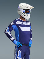 Pilota di motocross con maglia Alpinestars Racer Riway 2026 in UCLA Blue White, con marchio 'astars' sul petto, abbinata a pantaloni da motocross blu coordinati, casco bianco con maschera e guanti blu, abbigliamento da gara fuoristrada ad alte prestazioni