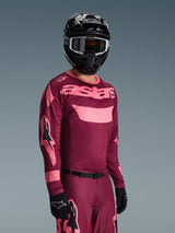 Pilota di motocross che indossa la maglia Alpinestars 2026 Racer Riway in Dark Red Coral con pantaloni coordinati, caratterizzata dal logo 'astars' rosa corallo sul petto, abbinata a un casco nero e guanti neri, set di abbigliamento da gara off-road coordinato.