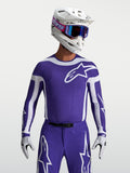 Alpinestars maglia Supertech Vesta, maglia da motocross da uomo, blu e bianco, in mesh elasticizzato con fori laser per ventilazione, indossata da un pilota con casco e guanti coordinati.