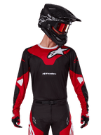 Alpinestars 2025 Racer Veil Jersey, maglia da motocross, nero e rosso acceso, indossata con pantaloni coordinati, casco nero e maschera rossa, caratterizzata da loghi bianchi e un design sportivo, abbigliamento tecnico per motocross off-road