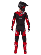 Pilota di motocross che indossa il completo Alpinestars Racer Veil 2025, maglia nera e rosso acceso con logo Alpinestars bianco, pantaloni coordinati, casco nero con occhiali rossi e stivali rossi, outfit completo per la guida fuoristrada