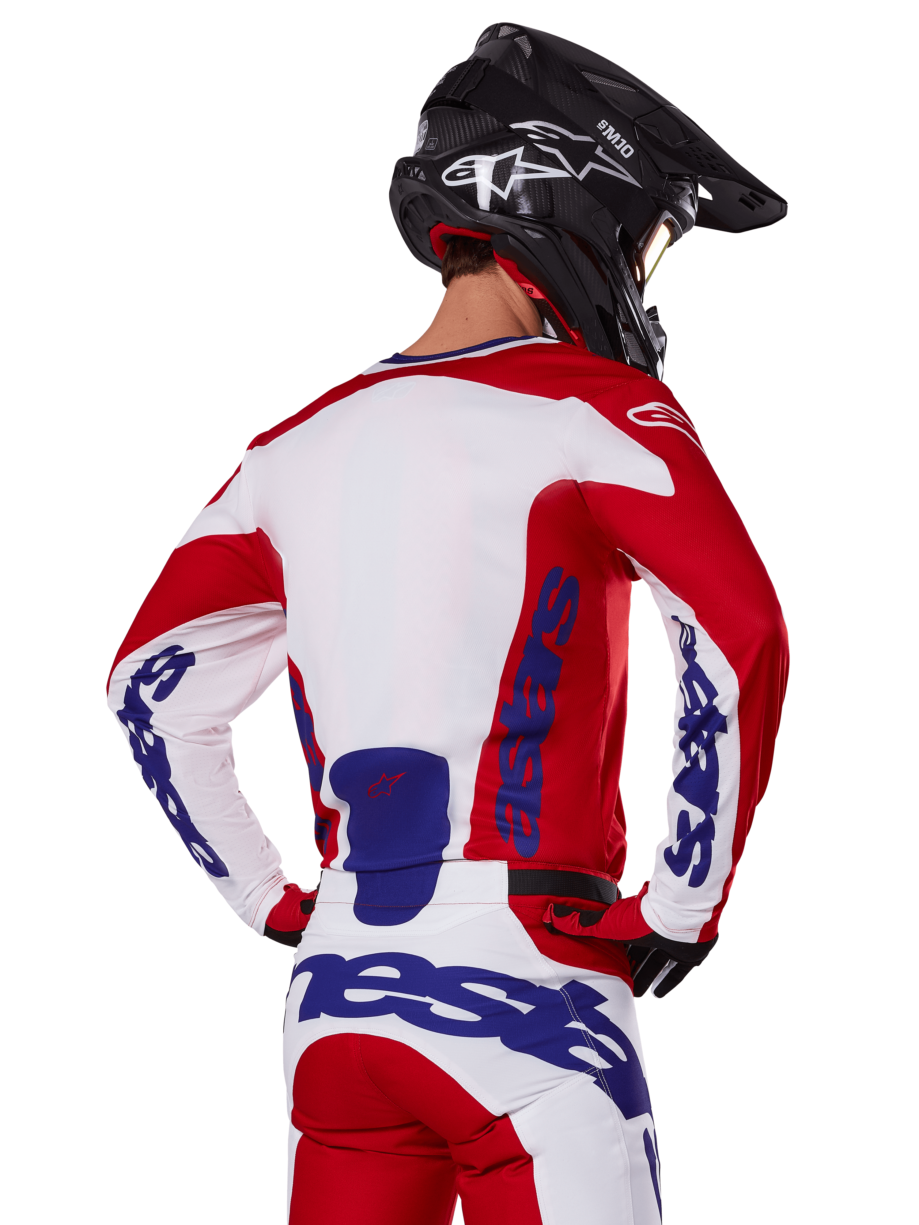 Maglia e pantaloni Alpinestars Racer Veil 2025, completo da motocross, rosso acceso, bianco e blu, vista posteriore del pilota che indossa il completo coordinato e un casco da motocross nero, con branding Alpinestars blu in evidenza, abbigliamento tecnico da corsa off-road