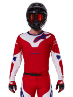 Maglia Alpinestars Racer Veil 2025, maglia da motocross, rossa, bianca e blu, a maniche lunghe, indossata con casco nero e maschera arancione, guanti e pantaloni rossi coordinati, design sportivo ad alte prestazioni per la guida fuoristrada