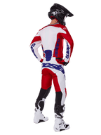 Pilota di motocross visto da dietro che indossa la maglia e i pantaloni Alpinestars Racer Veil 2025 in rosso e bianco, con loghi blu, casco nero e stivali bianchi, set completo di abbigliamento per corse fuoristrada