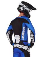Alpinestars 2025 Racer Veil Gear Set, abbigliamento da motocross, blu, nero e bianco, vista posteriore del pilota che indossa maglia e pantaloni con loghi evidenti, casco bianco e nero, completo coordinato per gare fuoristrada