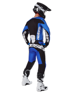 Pilota di motocross con abbigliamento completo da gara visto da dietro, maglia Racer Veil 2025 e pantaloni abbinati in blu e nero, con loghi Alpinestars bianchi, casco nero, stivali bianchi e neri, completo coordinato per gare off-road