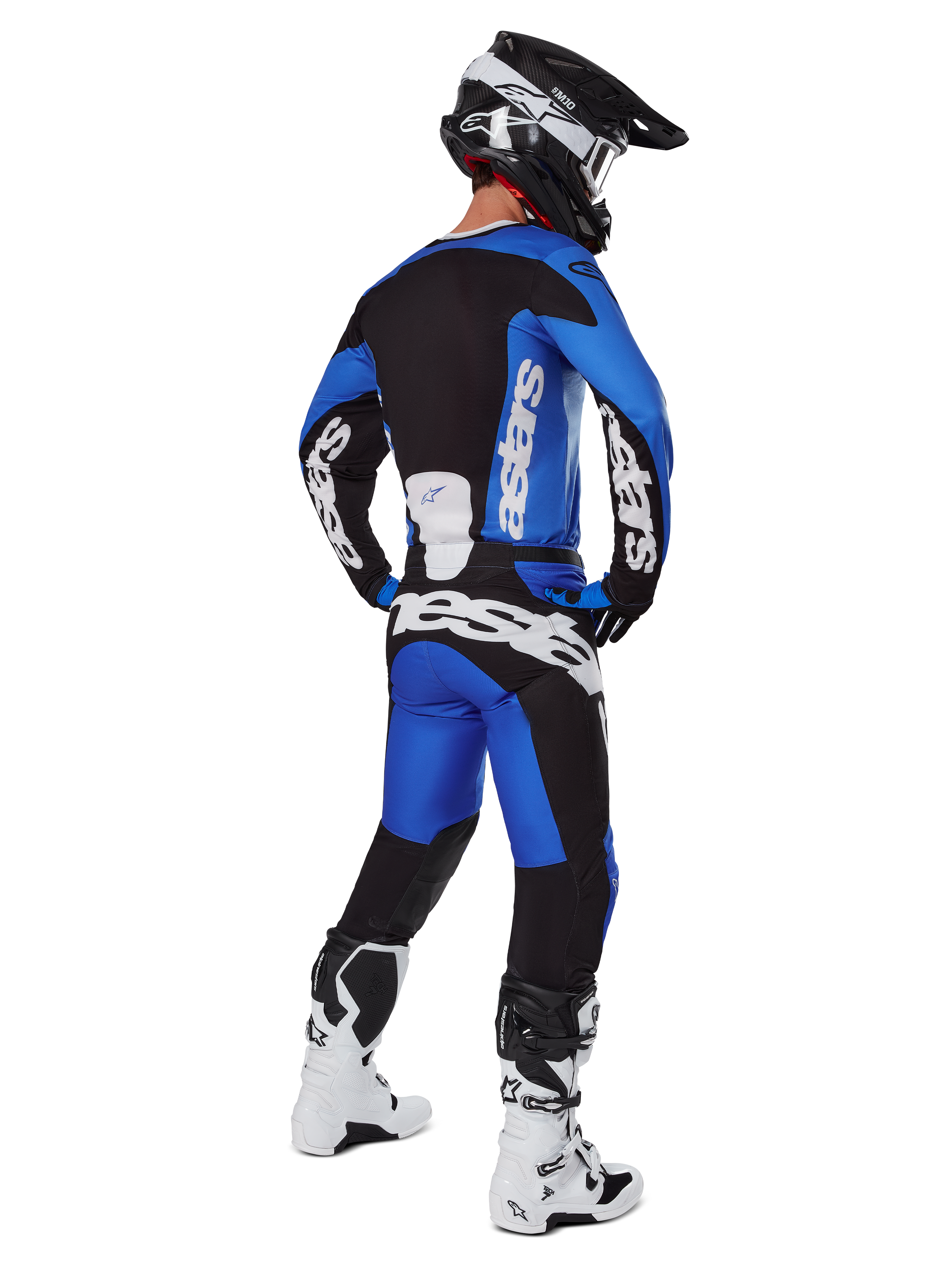 Pilota di motocross con abbigliamento completo da gara visto da dietro, maglia Racer Veil 2025 e pantaloni abbinati in blu e nero, con loghi Alpinestars bianchi, casco nero, stivali bianchi e neri, completo coordinato per gare off-road