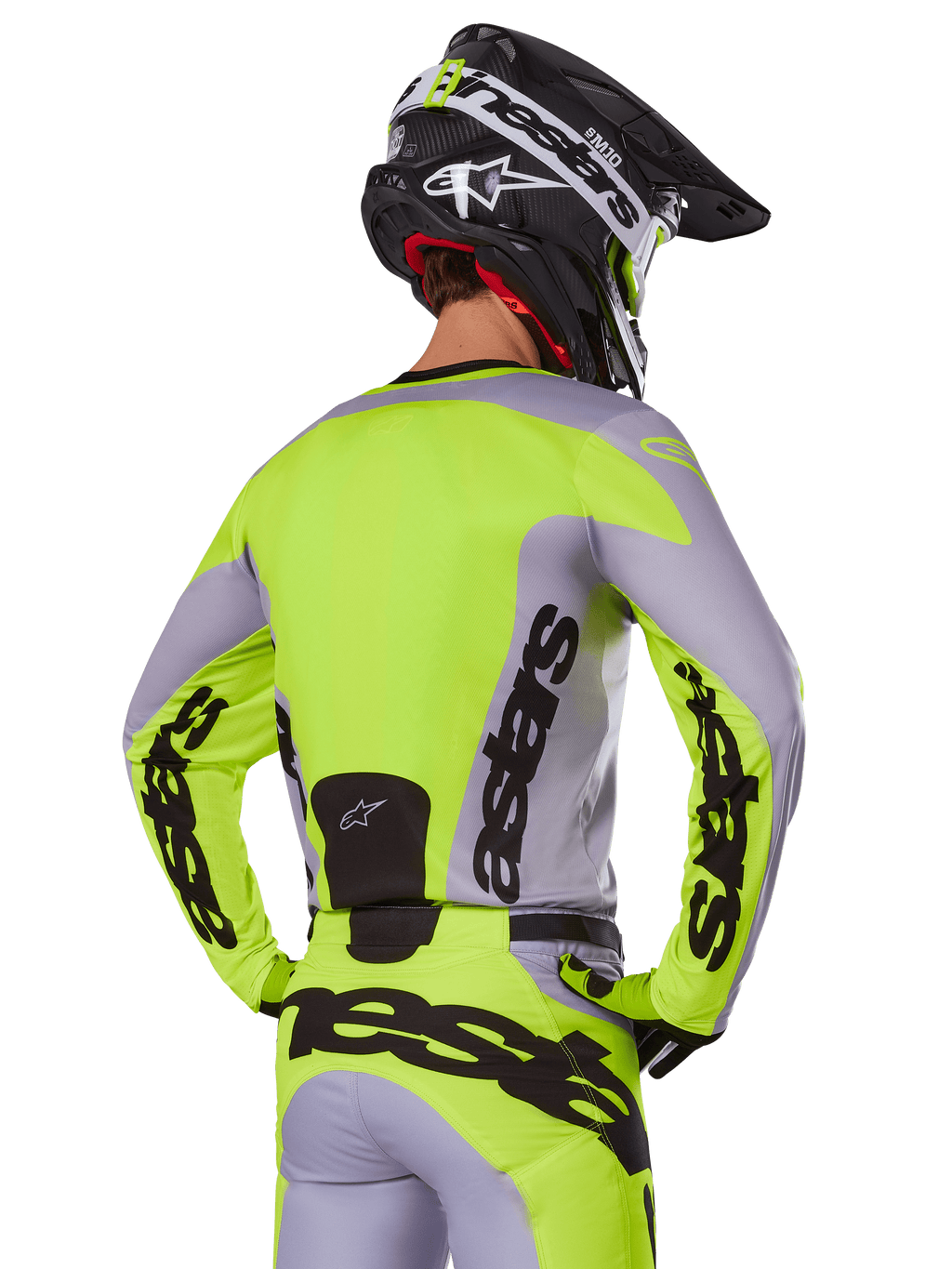 Pilota di motocross visto da dietro che indossa la maglia Alpinestars 2025 Racer Veil in grigio e giallo fluo, con l'evidente marchio 'astars' sulla schiena e sulle maniche, abbinata a pantaloni coordinati e un casco nero per un look racing completo.