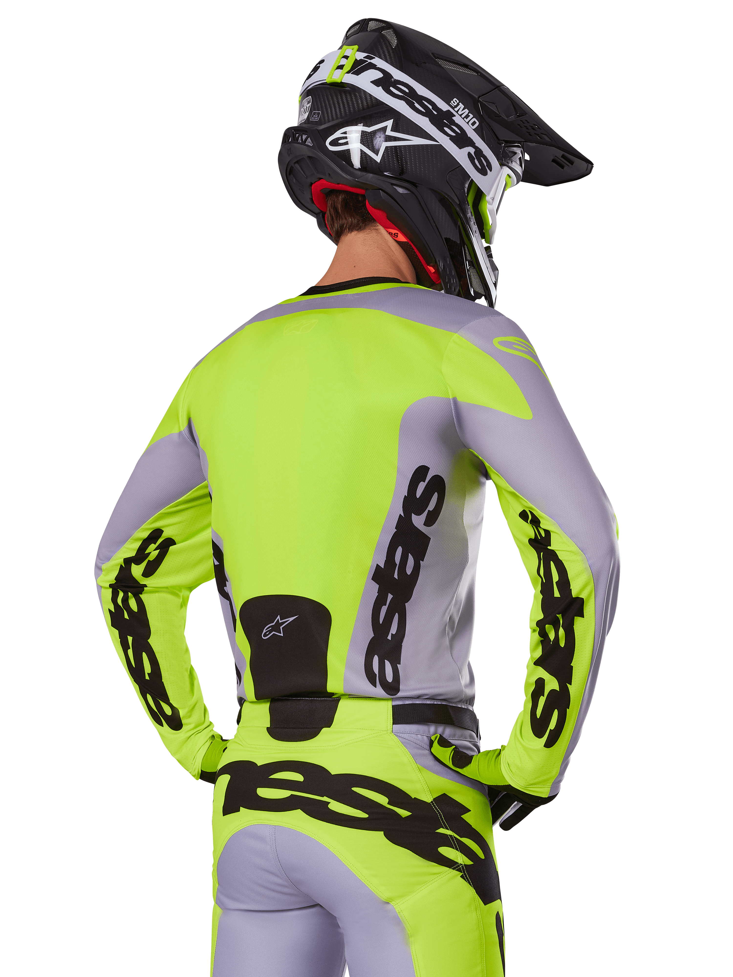 Pilota di motocross visto da dietro che indossa la maglia Alpinestars 2025 Racer Veil in grigio e giallo fluo, con l'evidente marchio 'astars' sulla schiena e sulle maniche, abbinata a pantaloni coordinati e un casco nero per un look racing completo.