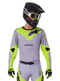 Alpinestars Racer Veil Jersey 2025, maglia da motocross, grigio e giallo neon, design a maniche lunghe con loghi Alpinestars neri, mostrata come parte di un set completo da gara con pantaloni coordinati, casco nero e guanti.