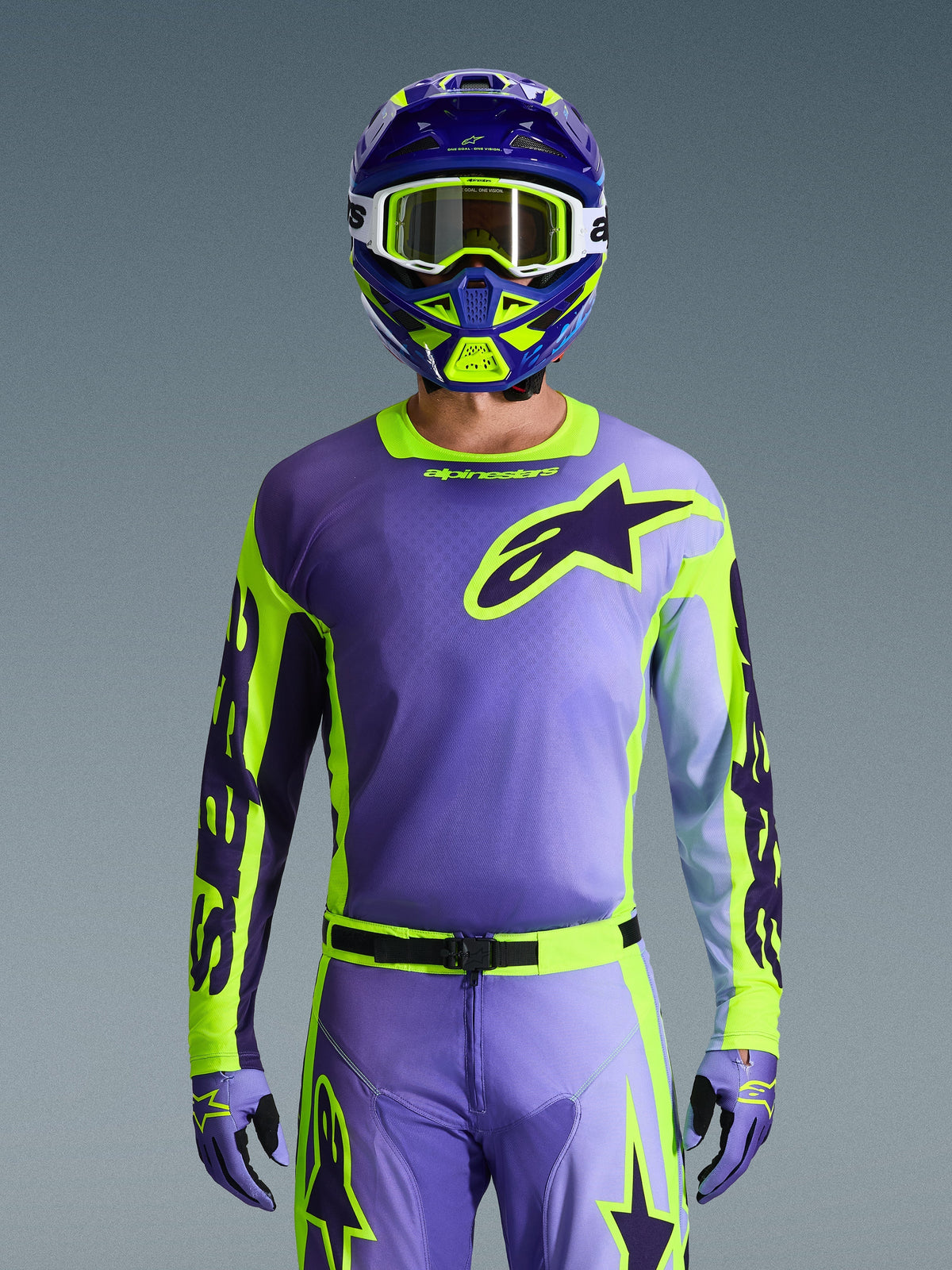 Maglia Alpinestars Racer Portl 2026, maglia da motocross, viola e giallo fluo, indossata con pantaloni da motocross, guanti e casco coordinati, con un grande logo a stella Alpinestars sul petto, scatto in studio su sfondo grigio