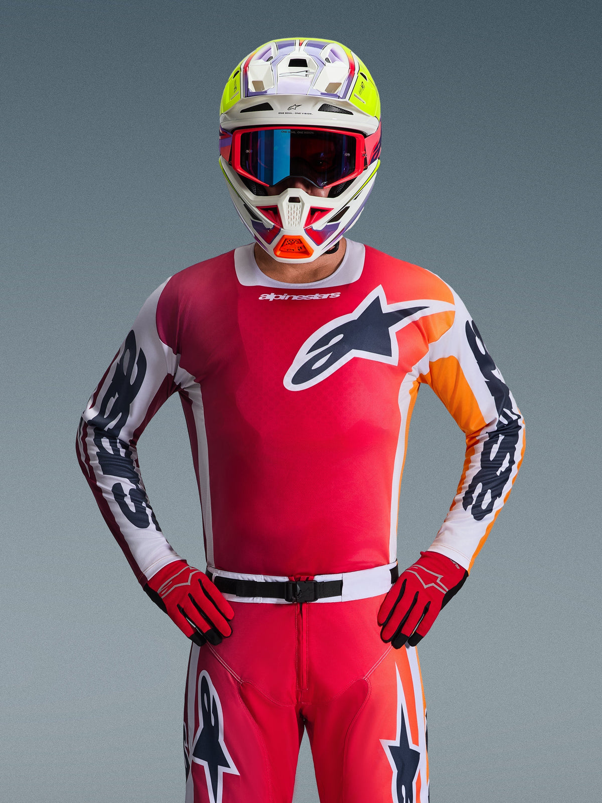 Alpinestars Racer Portl Jersey 2026, maglia da motocross rossa, vista frontale di un pilota che indossa pantaloni e guanti rossi coordinati, con logo a stella nero e bianco sul petto e maniche bianche con branding nero, abbinata a un casco multicolore bianco e giallo, abbigliamento professionale completo per corse fuoristrada.