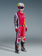 Pilota di motocross con il completo Alpinestars 2026 Racer Portl, maglia rossa e bianca con logo 'Astars' sulla manica, pantaloni rossi e bianchi coordinati, casco bianco e giallo con occhiali a montatura rossa e stivali da motocross grigi e neri, outfit completo per corse fuoristrada.