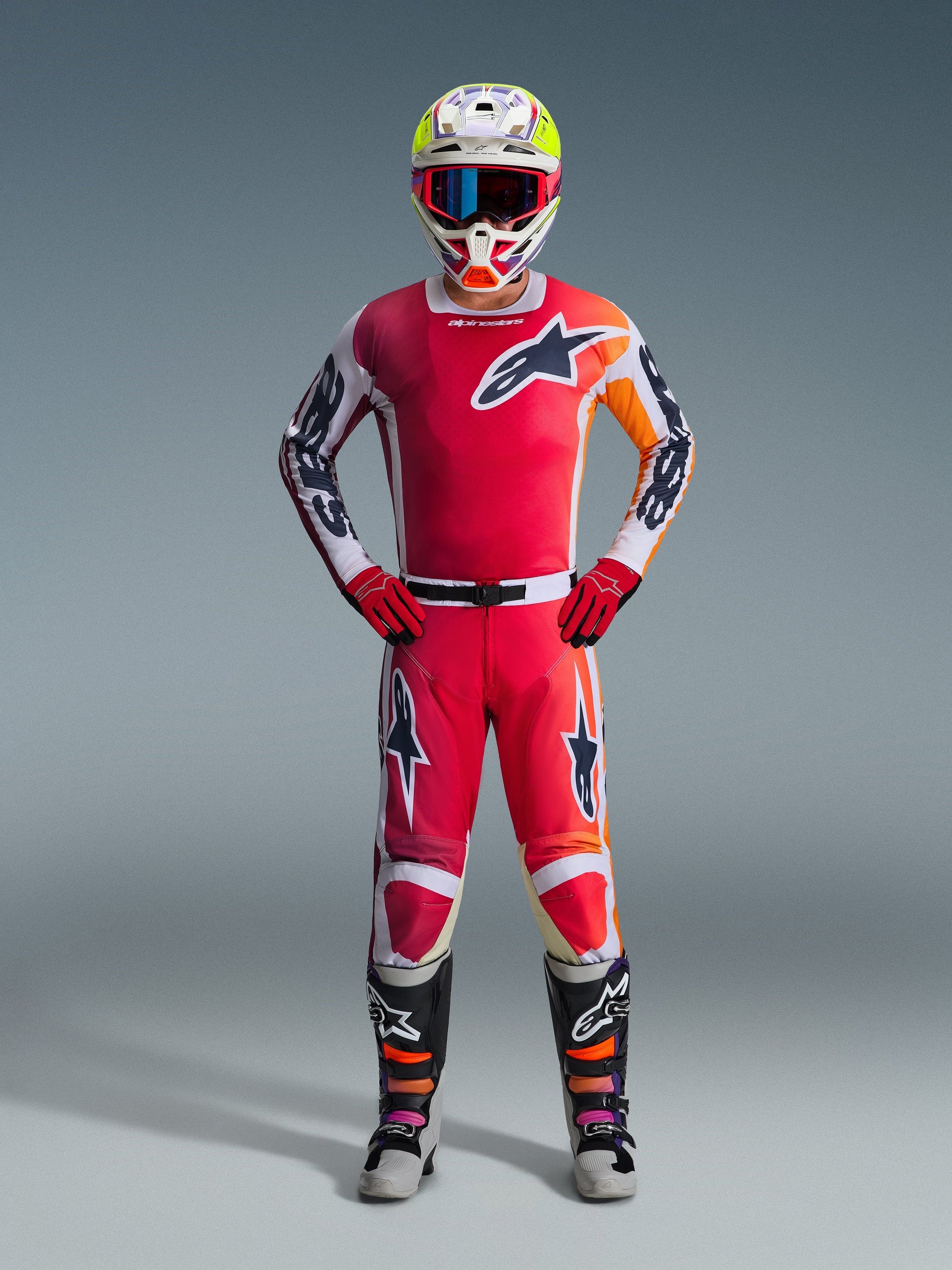 Pilota di motocross con maglia Alpinestars Racer Portl 2026 rossa, con dettagli grafici bianchi e arancioni, pantaloni da motocross coordinati, guanti rossi, casco da gara colorato con maschera e stivali tecnici bianchi e neri, set completo di equipaggiamento fuoristrada