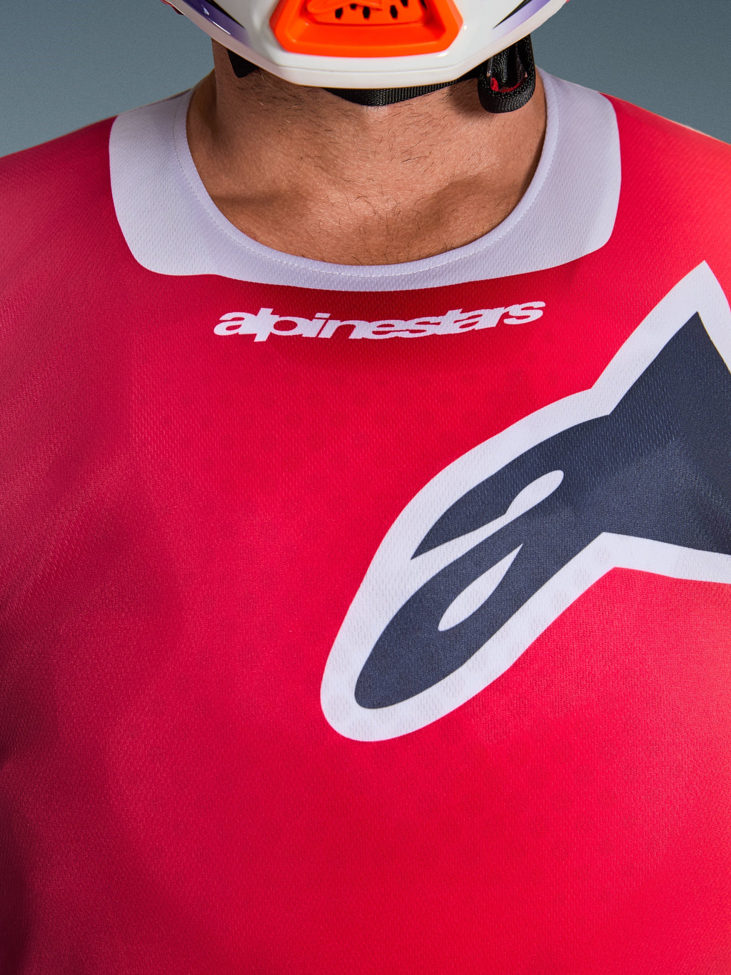 Maglia Alpinestars Racer Portl 2026, vista ravvicinata della zona del petto e del colletto, rossa con bordo del collo grigio chiaro, scritta Alpinestars bianca e grande logo Astars, caratterizzata da una trama in tessuto tecnico traspirante