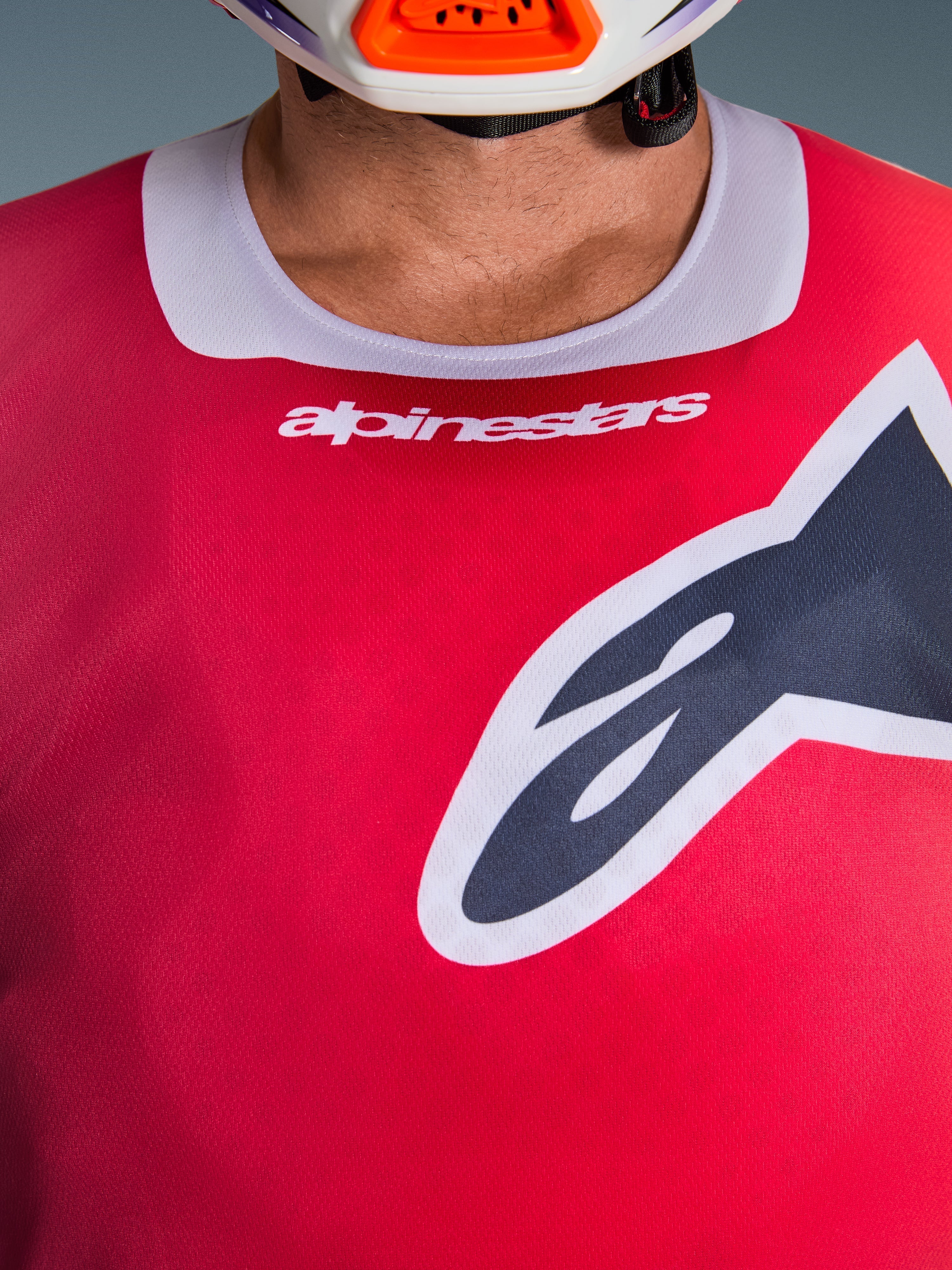 Maglia Alpinestars Racer Portl 2026, vista ravvicinata della zona del petto e del colletto, rossa con bordo del collo grigio chiaro, scritta Alpinestars bianca e grande logo Astars, caratterizzata da una trama in tessuto tecnico traspirante