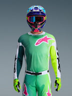 Alpinestars 2026 Racer Portl Gear Set, pilota di motocross con maglia sfumata verde e gialla e logo Astars rosa, pantaloni coordinati, casco colorato blu e rosa con maschera blu e guanti verde lime, completo professionale coordinato per corse off-road