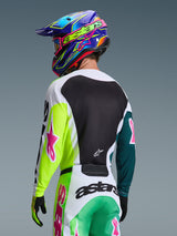 Pilota di motocross visto da dietro con la maglia Alpinestars Racer Portl 2026 in verde, bianco e nero, con loghi a stella rosa, abbinata a pantaloni coordinati e un casco colorato blu e viola, abbigliamento da gara coordinato per prestazioni fuoristrada.